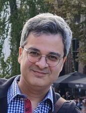 Dr. Amir Masoumi headshot, man with glasses and plaid shirt smiling